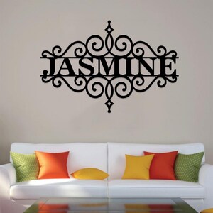 Pu&ograve; includere: Decorazione da parete in metallo nero con un design a volute decorative e il nome "JASMINE" al centro.