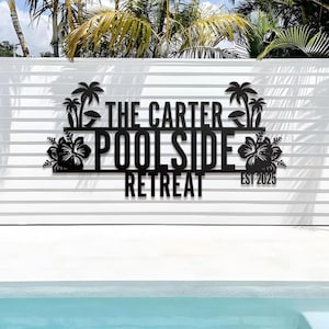 May include: Black metal sign reading "THE CARTER POOLSIDE RETREAT EST 2025". The sign has palm tree and hibiscus flower motifs. It's mounted on a white slatted wall, with a swimming pool visible in the foreground.