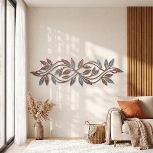 May include: A horizontal metal wall art piece featuring a symmetrical vine and leaf design. The metal has a weathered finish with a blend of rustic brown, copper, and oxidized teal green tones, creating a textured appearance across the foliage.