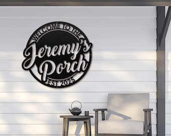 May include: Black metal sign that reads "Welcome to the Jeremy's Porch EST 2025" in a circular design. The sign is mounted on a white wall, with a porch setting including a chair and small table.