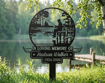 May include: Black metal memorial garden stake featuring a silhouette of a person fishing on a lake, framed by a circular design. The text "IN LOVING MEMORY OF Hudson Walker 1954-2026" is displayed below the scene, with wing accents.