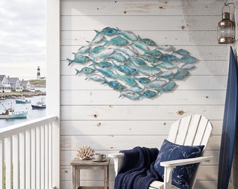 May include: A large metal wall sculpture depicting a school of fish in various shades of blue, teal, and white. The fish are arranged in a dense, overlapping horizontal formation, creating a sense of movement across the wall surface.