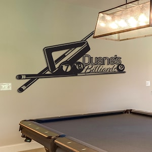 Può includere: Arte da parete in metallo nero con un biliardo, un triangolo e palle da biliardo con il testo "Duane's Billiards".