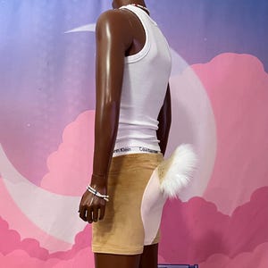 May include: A white ribbed vest top paired with tan shorts featuring a white panel on the back and a fluffy white tail attached. The vest top has a visible Calvin Klein waistband. The shorts are made of a soft, velvet-like fabric material.