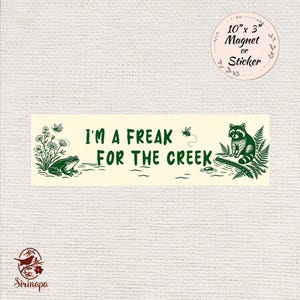 May include: A cream-colored magnet or sticker with the text "I'M A FREAK FOR THE CREEK" in green. The design includes a frog, flowers, a raccoon, and a fly. The magnet measures 10 inches by 3 inches.