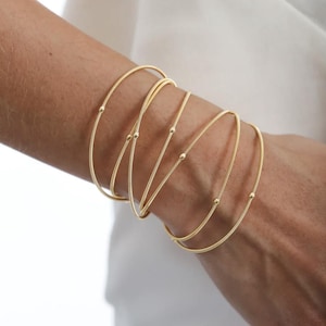 Könnte beinhalten: Ein Set aus fünf goldenen Armreifen mit kleinen Perlen an jedem Armreif.