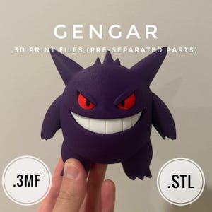 以下が含まれることがあります： 赤い目と大きな歯並びの笑顔を持つ紫色のゲンガーのフィギュア。「GENGAR」の文字がフィギュアの上にあり、その下に「3D PRINT FILES (PRE-SEPARATED PARTS)」と書かれています。フィギュアは手で持たれています。.3MFと.STLのファイル形式も表示されています。