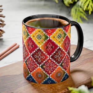 May include: A ceramic coffee mug with a black handle and rim. The mug features a colorful, geometric pattern in red, yellow, orange, and blue. The mug is filled with a hot beverage, and steam is rising from the top.