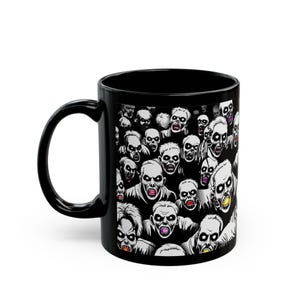 May include: Black ceramic coffee mug featuring a crowd of zombie faces in shades of gray, white, and black. The zombie faces have open mouths and exposed teeth. The mug has a black handle and a glossy finish.