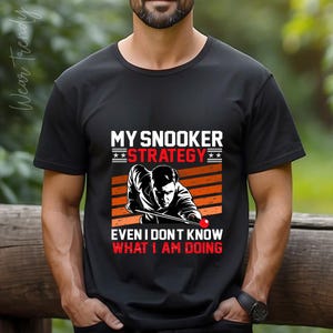 May include: A black t-shirt with a white graphic of a person playing snooker. The text on the shirt reads "My Snooker Strategy Even I Don't Know What I Am Doing."