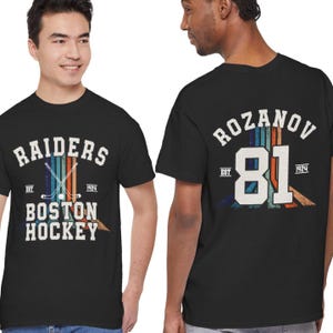 Könnte beinhalten: Schwarzes T-Shirt mit dem Text "RAIDERS BOSTON HOCKEY" und gekreuzten Hockeyschlägern. Auf der Rückseite steht "ROZANOV 81" mit Vintage-Design. Das Shirt enthält "EST 1924" auf beiden Seiten.