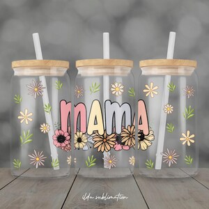 May include: Three clear glass tumblers with wooden lids and white straws. Each tumbler features the word "MAMA" in pastel colours, surrounded by floral designs. The tumblers are decorated with daisies and green leaves. The text "ilda sublimation" is at the bottom.