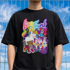 Puede incluir: Camiseta negra con un diseño gráfico colorido de "Lisa Frank". El diseño incluye un unicornio, un tigre, un panda y conejos. El gráfico tiene acentos de arcoíris y colores pastel.