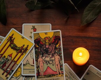 May include: A collection of tarot cards with colorful illustrations, including the Four of Wands and The Lovers, are arranged on a dark wooden surface. A lit candle provides a warm glow, enhancing the mystical theme.