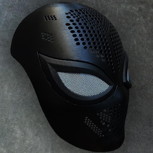 Op de afbeelding: Een zwart plastic masker met een spinnenwebontwerp en een gaasoogbedekking. Het masker heeft een getextureerd oppervlak met kleine gaatjes.