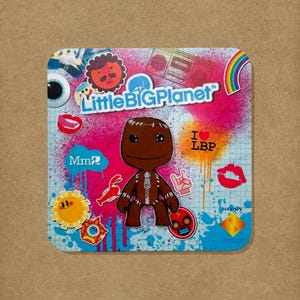 Könnte beinhalten: Ein quadratischer Aufkleber mit einer braunen Sackboy-Figur aus LittleBigPlanet in der Mitte. Der Hintergrund ist eine lebendige Collage aus rosa und blauem Sprühlack, einem Regenbogen, einer Sonne, Lippen und dem Text LittleBigPlanet, Mm und Sony.