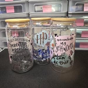 May include: Three glass beverage jars with wooden lids. Each jar has a different design with text and graphics. One jar says "Fully Broken Perfectly Imperfect". Another features a "HP" logo. The third says "I acknowledge my Selfworth".