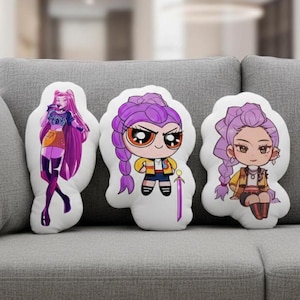 May include: Three white decorative pillows with cartoon character designs. The pillows feature characters with purple hair, wearing various outfits. The pillows are arranged on a gray couch.