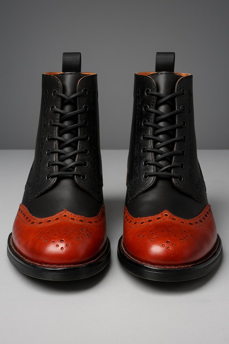 May include: A pair of two-tone leather boots. The upper portion is black, while the toe and lower section are a reddish-brown. The boots have a lace-up design with black laces and a decorative pattern on the toe.