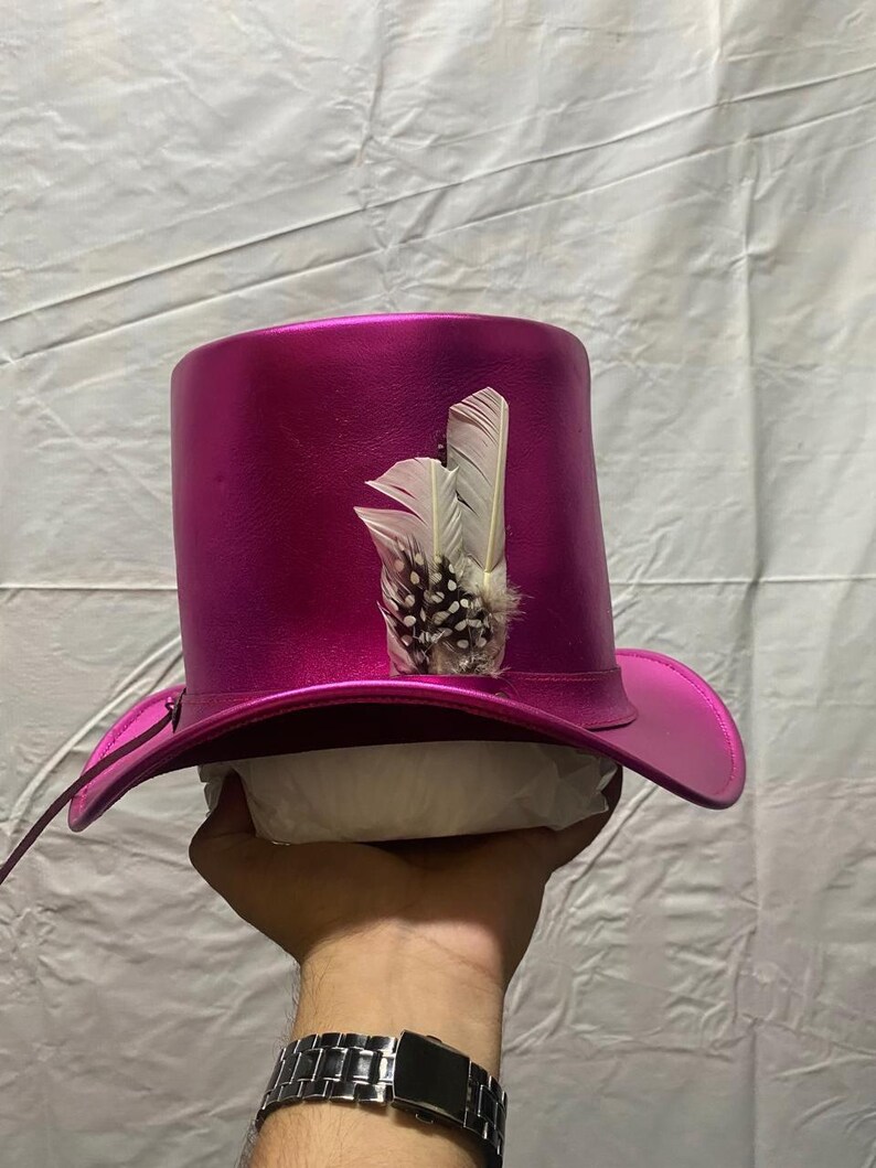 May include: A magenta top hat with a wide brim and a decorative feather accent. The hat has a shiny finish and a classic top hat shape. The feather is white with a speckled pattern.