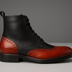 May include: A two-tone leather boot with a classic design. The upper is black, while the toe and heel counter are a rich reddish-brown. Features include brogue detailing and a lace-up closure. The boot has a sturdy black sole.