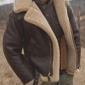 Puede incluir: Chaqueta de cuero marrón con forro y cuello de borrego beige. La chaqueta tiene cierre de cremallera, una correa con hebilla en la cintura y una estética cálida y robusta. Una prenda de abrigo clásica.