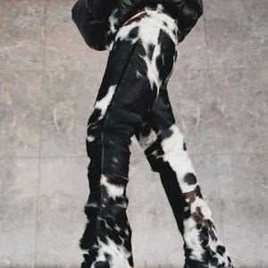Peut inclure: Pantalon &agrave; motif de peau de vache noir et blanc. Le pantalon est taille haute et &eacute;vas&eacute;. La mati&egrave;re est douce et textur&eacute;e. L'ensemble est compl&eacute;t&eacute; par des chaussures noires et une veste noire.