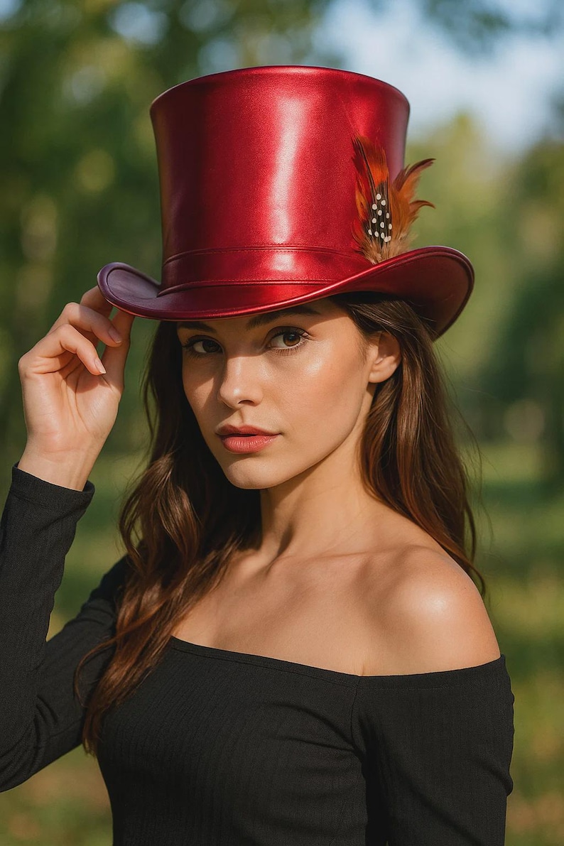 May include: A shiny red top hat with a wide brim and a decorative feather. The hat is the focal point, with a woman's hand gently touching the brim. The background is a blurred green, suggesting an outdoor setting.