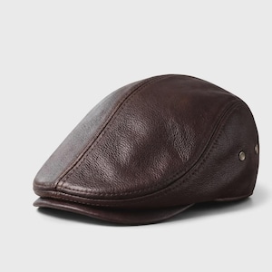 Puede incluir: Gorra plana de cuero marrón oscuro. Presenta una corona redondeada, una pequeña visera y una superficie texturizada. Dos pequeños remaches metálicos son visibles en el lateral. Un sombrero clásico para diversas ocasiones.