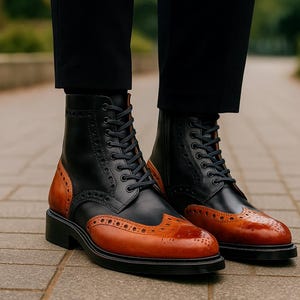 May include: Black and brown leather ankle boots with a wingtip design. The boots have a lace-up closure, a rounded toe, and a black sole. The brown leather is on the toe and heel, while the rest of the boot is black.