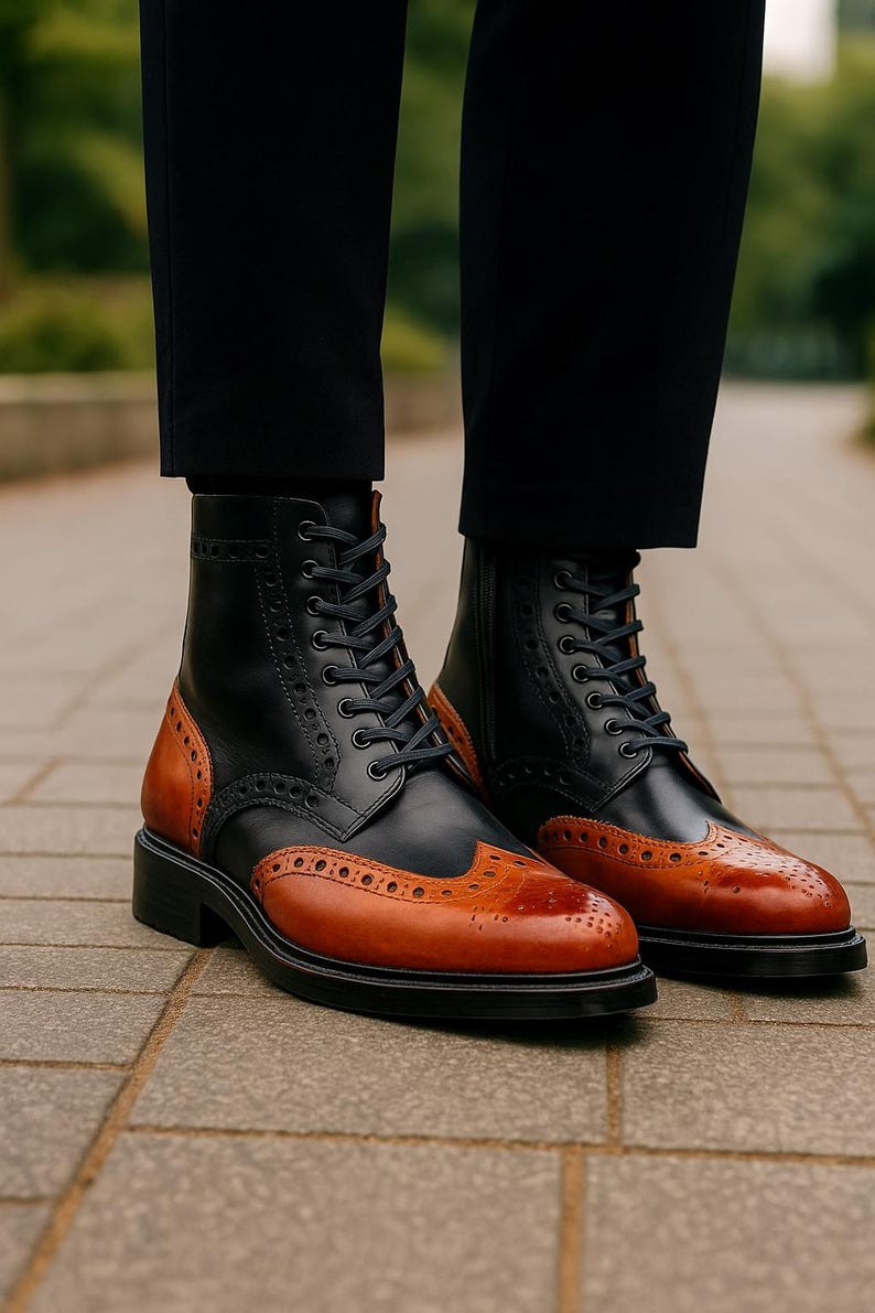 May include: Black and brown leather ankle boots with a wingtip design. The boots have a lace-up closure, a rounded toe, and a black sole. The brown leather is on the toe and heel, while the rest of the boot is black.