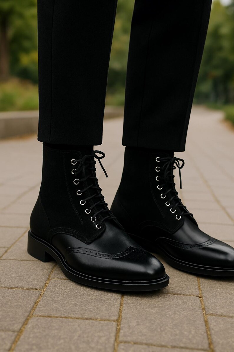 May include: Black leather ankle boots with a lace-up design and brogue detailing. The boots have a suede panel at the top and are worn with black trousers. The boots have a low heel.