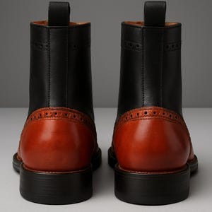 May include: A pair of two-tone leather boots. The boots have a black upper and a brown heel and toe. The boots have a pull tab at the top and a decorative pattern around the heel. The soles are black.