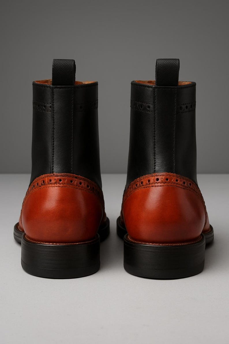May include: A pair of two-tone leather boots. The boots have a black upper and a brown heel and toe. The boots have a pull tab at the top and a decorative pattern around the heel. The soles are black.