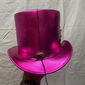 Pode incluir: Um chap&eacute;u alto rosa choque brilhante com aba larga. O chap&eacute;u apresenta um fecho decorativo cor de bronze e um fino cord&atilde;o de couro castanho escuro. O chap&eacute;u &eacute; feito de um material liso e refletor. Um acess&oacute;rio vibrante.