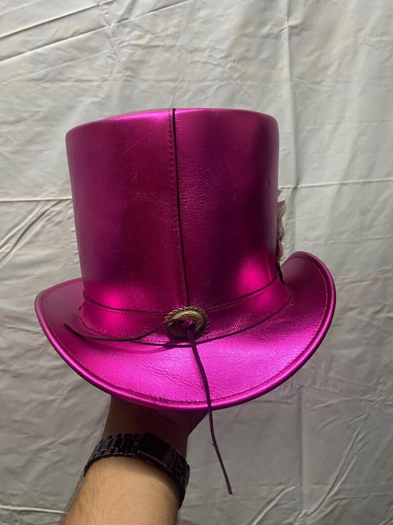 Pode incluir: Um chap&eacute;u alto rosa choque brilhante com aba larga. O chap&eacute;u apresenta um fecho decorativo cor de bronze e um fino cord&atilde;o de couro castanho escuro. O chap&eacute;u &eacute; feito de um material liso e refletor. Um acess&oacute;rio vibrante.