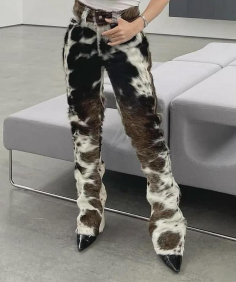 Peut inclure: Pantalon &agrave; motif de peau de vache avec une ceinture en cuir marron et des talons noirs &agrave; bout pointu. Le pantalon pr&eacute;sente un design unique avec des taches noires, marron et blanches, cr&eacute;ant un look distinctif.