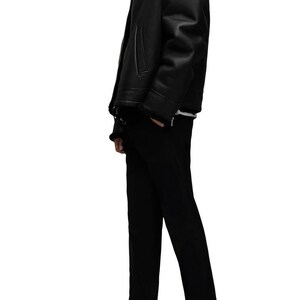K&ouml;nnte beinhalten: Schwarze Lederjacke mit Shearling-Kragen, kombiniert mit schwarzer Hose und schwarzen Lederstiefeln. Die Jacke hat einen Rei&szlig;verschluss und Seitentaschen. Das Outfit ist ein klassisches, ganz schwarzes Ensemble.