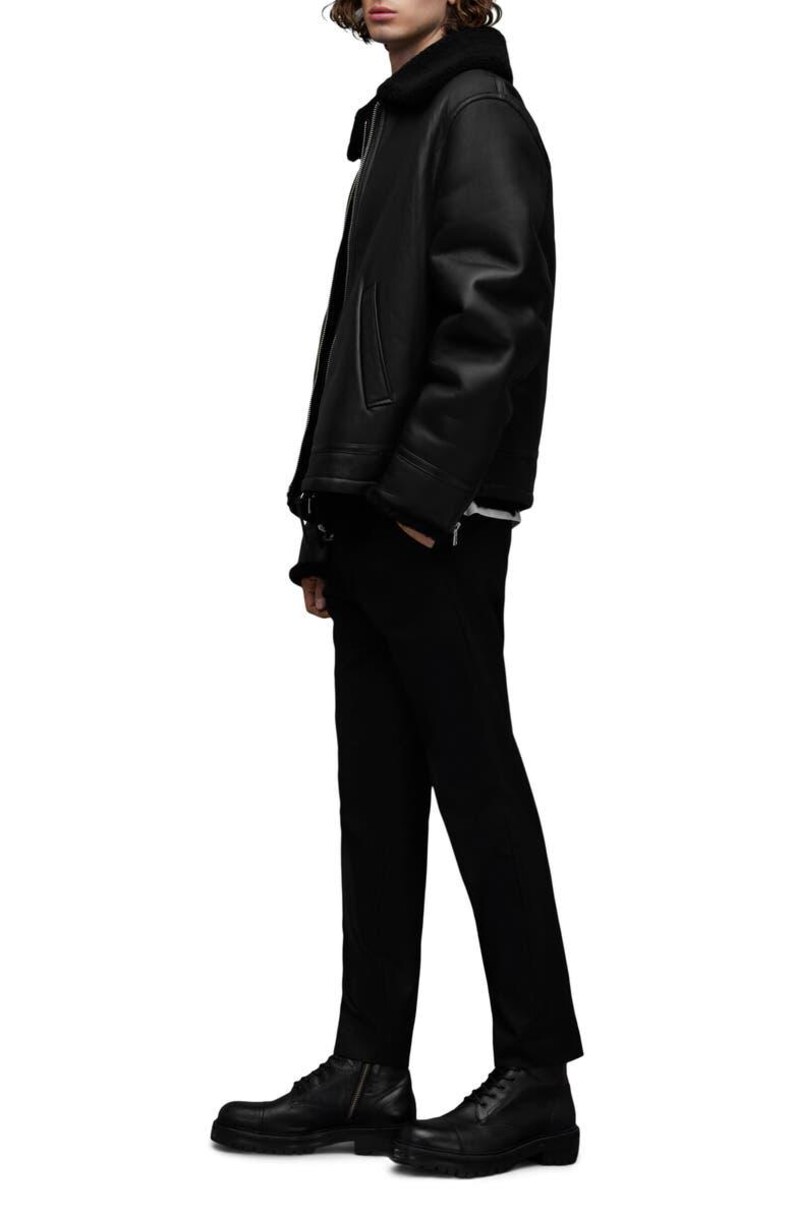 K&ouml;nnte beinhalten: Schwarze Lederjacke mit Shearling-Kragen, kombiniert mit schwarzer Hose und schwarzen Lederstiefeln. Die Jacke hat einen Rei&szlig;verschluss und Seitentaschen. Das Outfit ist ein klassisches, ganz schwarzes Ensemble.