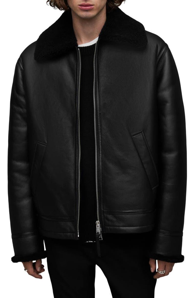 K&ouml;nnte beinhalten: Schwarze Lederjacke mit Shearling-Kragen und -Futter. Die Jacke hat einen Rei&szlig;verschluss vorne, zwei Seitentaschen und Shearling-Besatz an den Manschetten. Ein klassischer Stil, geeignet f&uuml;r kaltes Wetter.