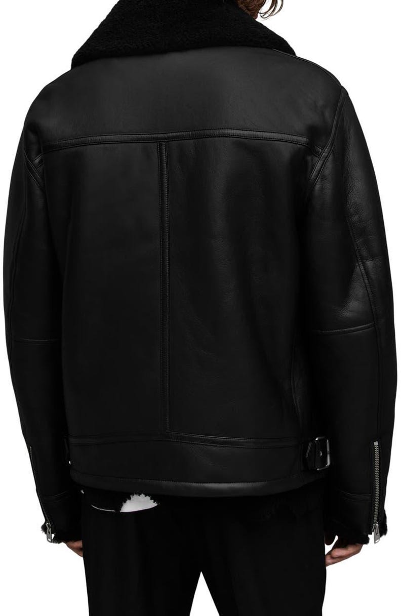K&ouml;nnte beinhalten: Schwarze Lederjacke mit Shearling-Kragen. Die Jacke hat einen Rei&szlig;verschluss, eine Schnalle an der Taille und Rei&szlig;verschlussmanschetten. Die R&uuml;ckseite der Jacke hat ein klassisches Design mit vertikalen N&auml;hten.