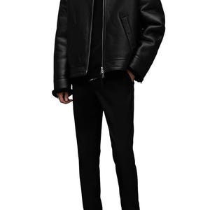 K&ouml;nnte beinhalten: Schwarze Lederjacke mit Shearling-Kragen, kombiniert mit schwarzer Hose und Stiefeln. Die Jacke hat einen Rei&szlig;verschluss vorne und ein klassisches Design. Ein komplettes Outfit f&uuml;r einen stilvollen Look.