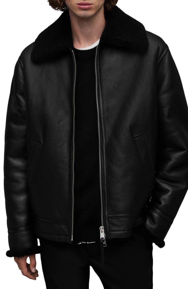 K&ouml;nnte beinhalten: Schwarze Lederjacke mit schwarzem Shearling-Kragen und -Futter. Die Jacke hat einen silbernen Rei&szlig;verschluss, zwei Vordertaschen und Shearling-Besatz an den Manschetten. Ein klassisches Oberbekleidungsst&uuml;ck.