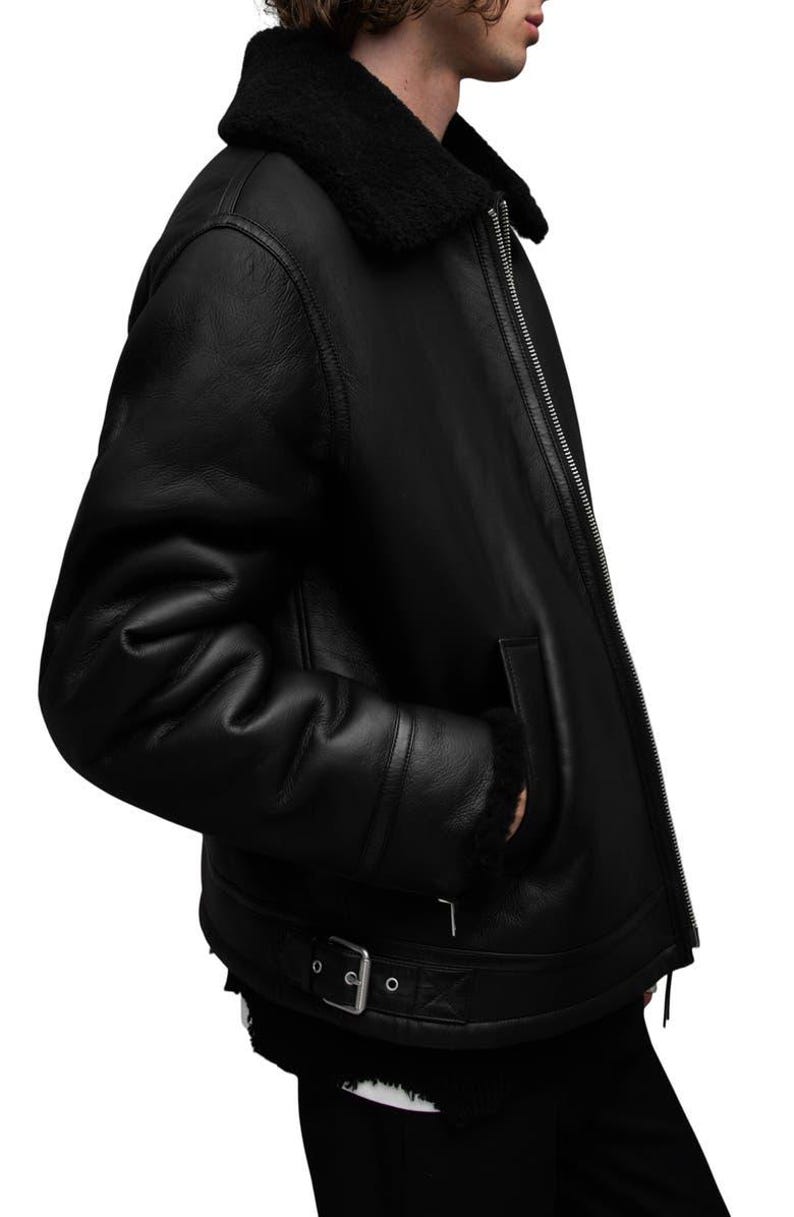 K&ouml;nnte beinhalten: Schwarze Lederjacke mit Shearling-Kragen und -Futter. Die Jacke hat einen Rei&szlig;verschluss, Seitentaschen und einen Schnallenriemen an der Taille. Ein klassisches Oberbekleidungsst&uuml;ck.