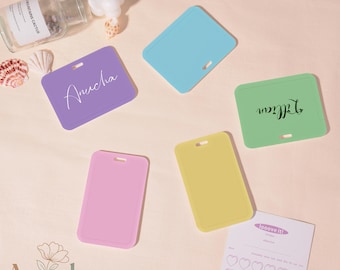 May include: A collection of colorful ID badge holders in lavender, blue, green, pink, and yellow. Some holders have names written on them in cursive. A small notepad with heart-shaped stickers is also visible.