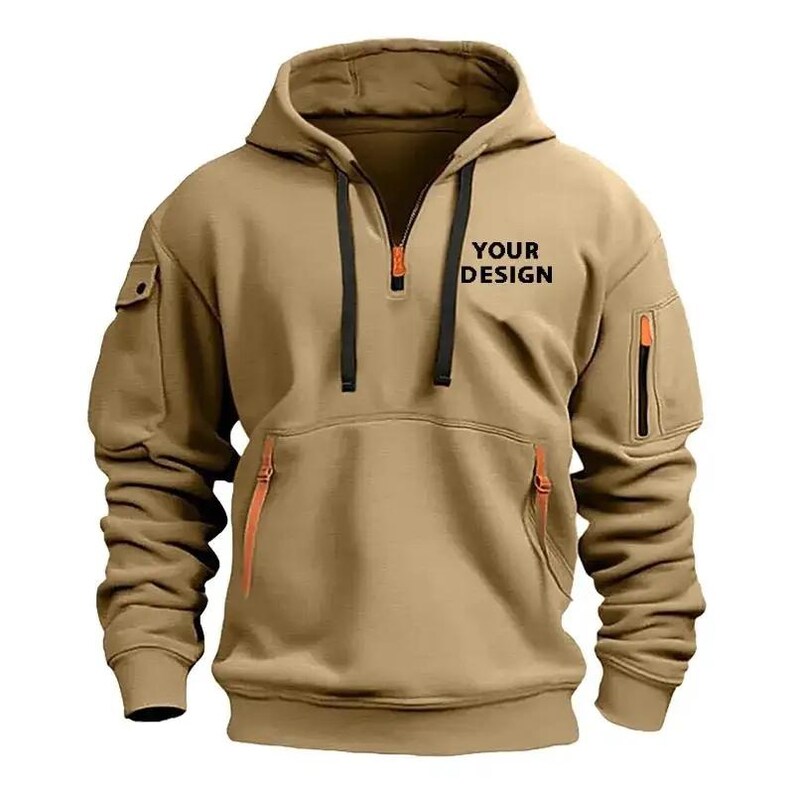 May include: A tan hooded sweatshirt with a half-zip closure and multiple pockets. The sweatshirt features black drawstrings and orange zipper accents. The text "YOUR DESIGN" is printed on the chest. This casual outerwear is suitable for various activities.