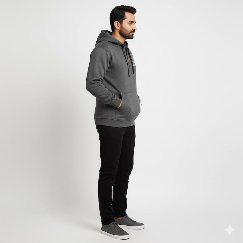 May include: A charcoal gray hoodie with a drawstring hood and a kangaroo pocket. The hoodie has a small logo on the chest and a zipper detail on the pocket. The person is wearing black pants and gray sneakers.