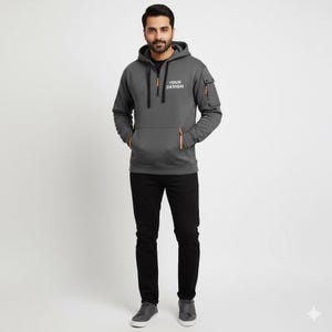 Personalised Logo Hoodies, Custom Logo Hoodie, Company Merch Jumpers, Custom Workwear Gift for Worker, Uniform Hoodie, Gift for Dad. May include: A charcoal gray hoodie with a front pocket and a zippered chest. The hoodie has a drawstring hood and a small pocket on the left sleeve. The text "YOUR DESIGN" is printed on the chest. The person is wearing black pants and gray sneakers.