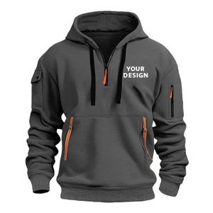 Personalised Logo Hoodies, Custom Logo Hoodie, Company Merch Jumpers, Custom Workwear Gift for Worker, Uniform Hoodie, Gift for Dad. May include: A charcoal gray hoodie with a drawstring hood and a half-zip Customizable hoodie in black. Available in different colors and personalized sizes closure. The hoodie features a kangaroo pocket, a small pocket on the left sleeve, and two zippered pockets. The text "YOUR DESIGN" is printed on the chest. The zipper pulls and pocket accents are orange.