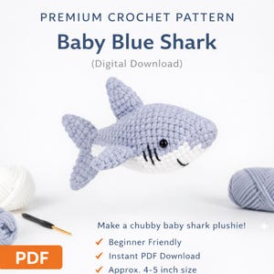May include: A crocheted baby shark plushie in pale blue and white, with black detailing. The image includes the text "Baby Blue Shark" and "Premium Crochet Pattern". The plushie is approximately 10-13 cm in size.